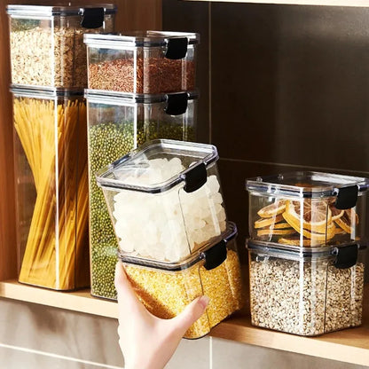 A collection of transparent storage containers filled with various dry foods like pasta, beans, nuts, and cereals on a wooden surface.